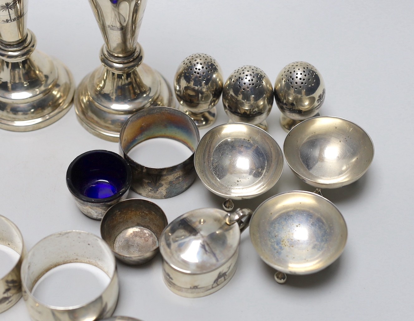 Thirteen assorted Iraq white metal and niello condiments, circular box, five similar napkin rings, a brooch and a pair of similar (damaged) candlesticks.